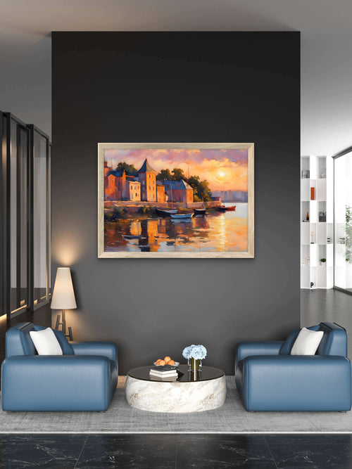 A framed landscape oil painting of a sunset over a lake with boats and colorful buildings, displayed on a dark gray wall in a modern living room setting with blue armchairs and a marble coffee table.