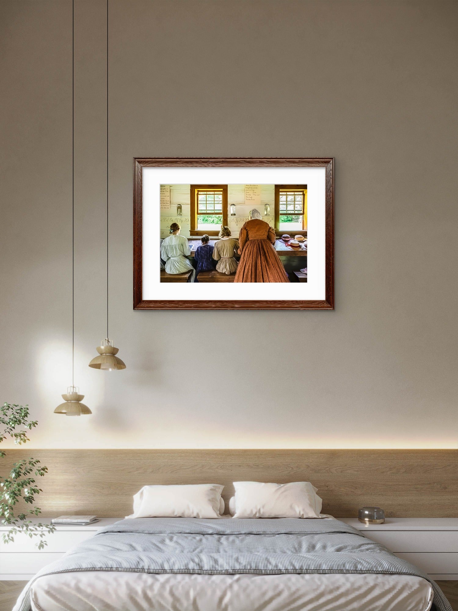 A framed art print depicting a scene with people in a room, styled on a beige wall above a bed in a modern bedroom setting.