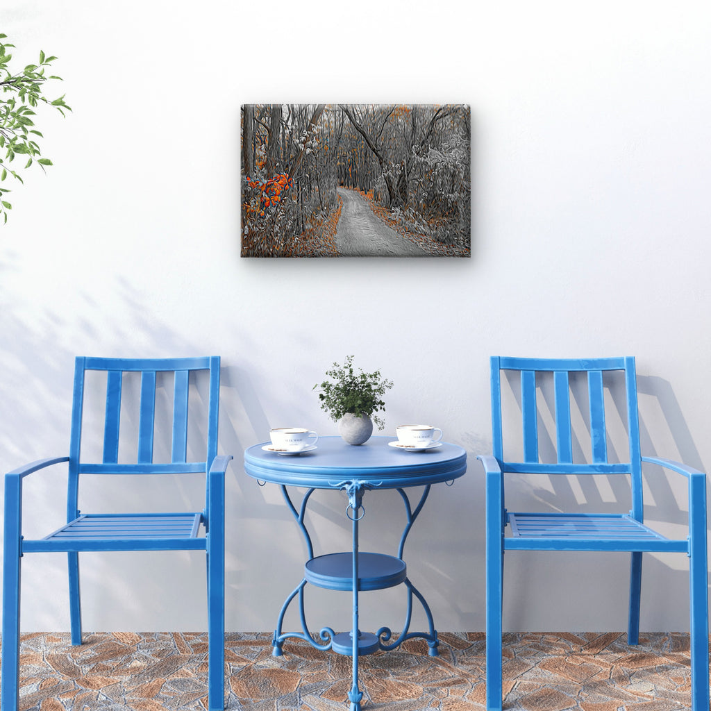 A rectangular wall art print showing a forest path in muted gray, white, and orange tones, displayed above a small round table with two blue chairs in a styled interior scene.