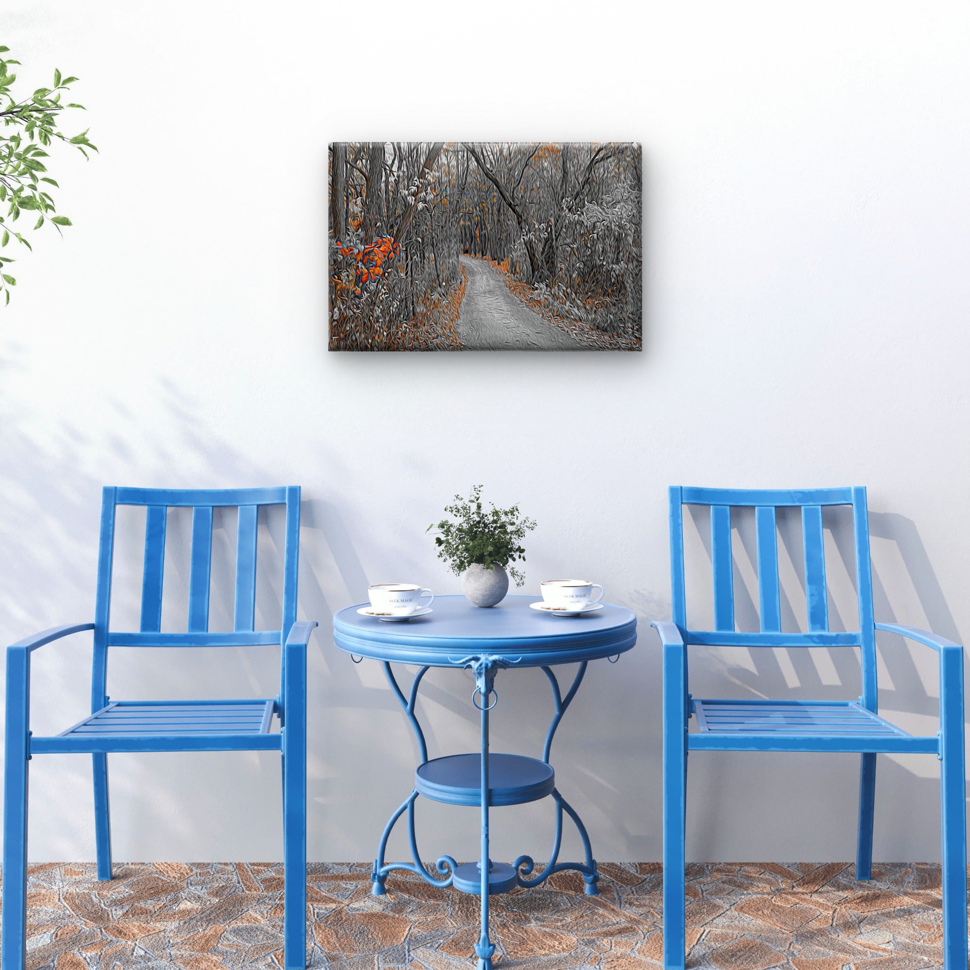 A rectangular wall art print showing a forest path in muted gray, white, and orange tones, displayed above a small round table with two blue chairs in a styled interior scene.