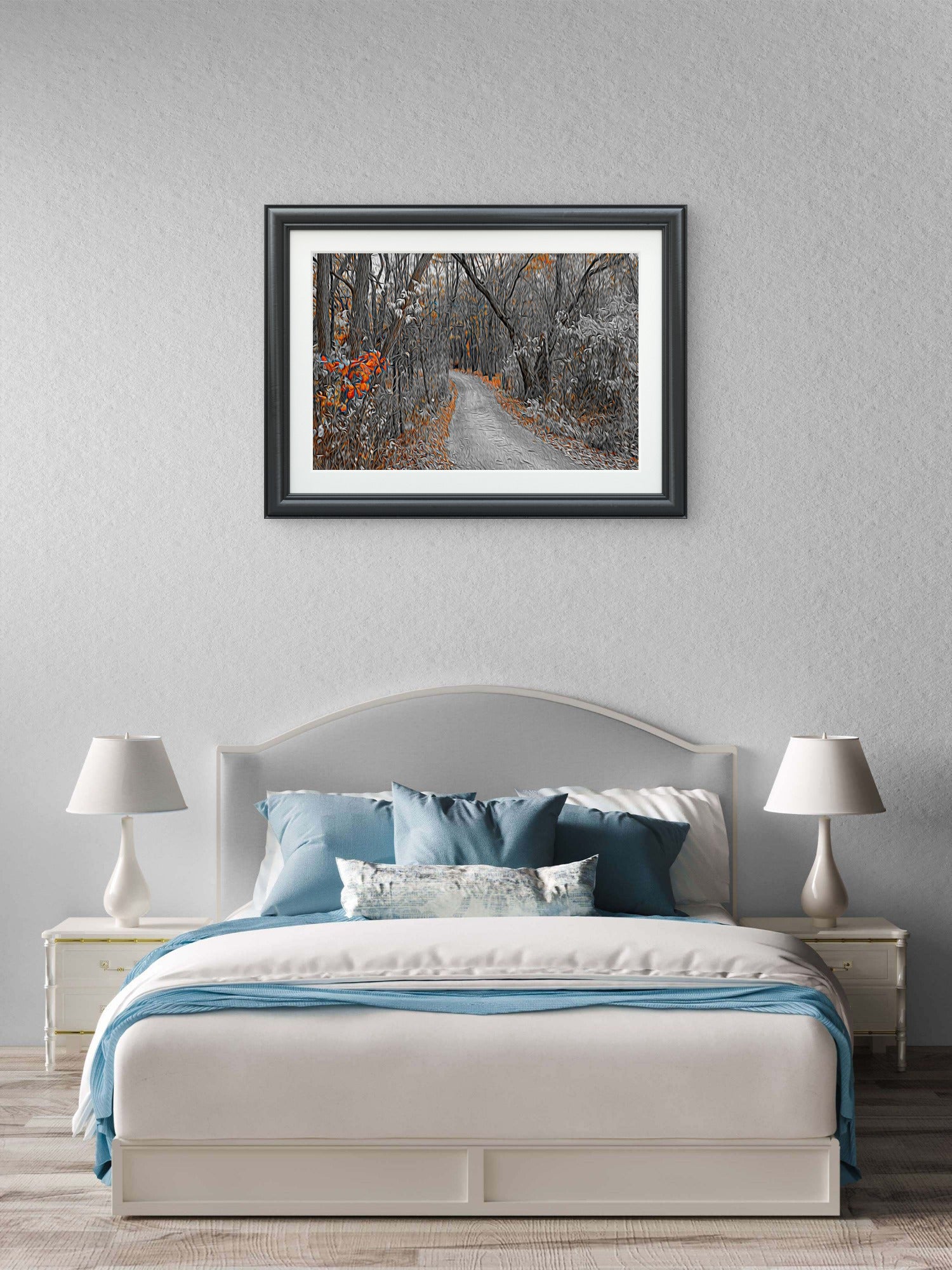 A framed landscape art print of a snowy forest path with orange autumn leaves, displayed on a textured light gray wall above a neatly made bed in a modern bedroom setting.